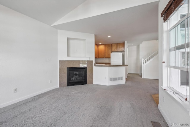 unfurnished living room featuring light carpet, a tiled fireplace, and vaulted ceiling