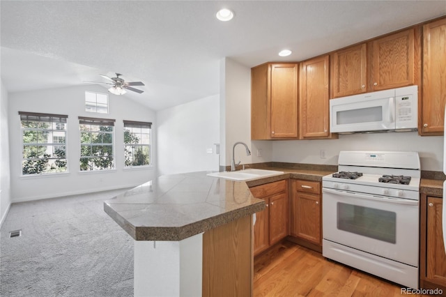 kitchen featuring kitchen peninsula, vaulted ceiling, light hardwood / wood-style flooring, sink, and white appliances