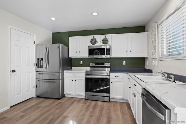 kitchen featuring appliances with stainless steel finishes, white cabinetry, light wood-style floors, and a sink