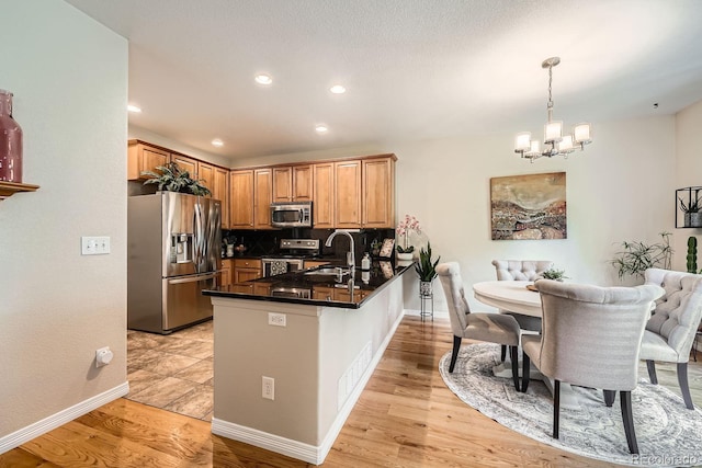 11839 E Fair Ave, Greenwood Village, CO 80111 - kitchen featuring appliances with stainless steel finishes, a peninsula, dark countertops, a chandelier, and decorative backsplash