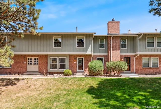 view of front of property with a front yard, a chimney, brick siding, board and batten siding, and entry steps
