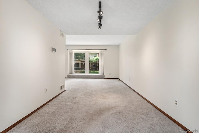 unfurnished room with carpet floors, baseboards, rail lighting, and visible vents
