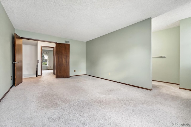 empty room featuring baseboards, light colored carpet, a textured ceiling, and visible vents