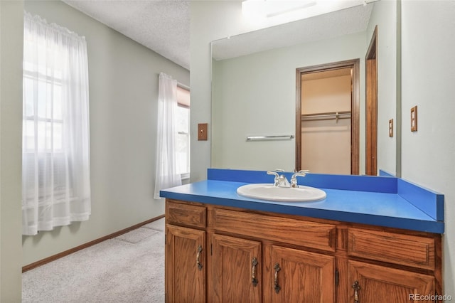 bathroom with vanity, a textured ceiling, baseboards, and a spacious closet