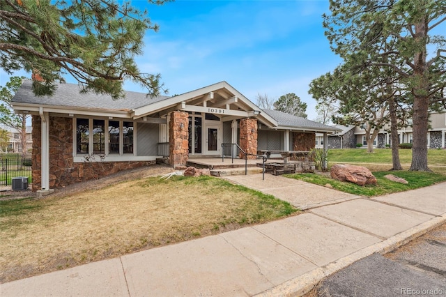 view of front of house with a shingled roof, a front lawn, stone siding, cooling unit, and covered porch