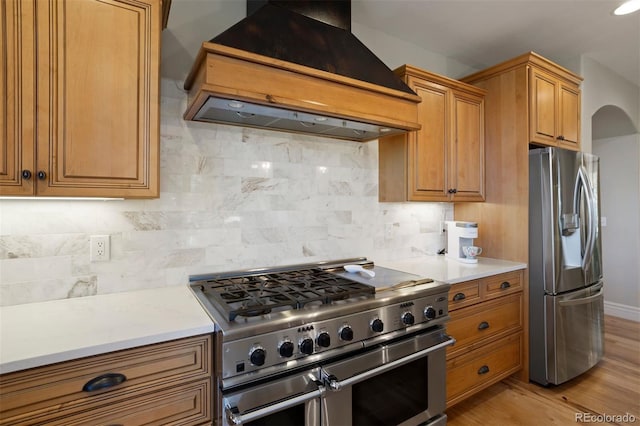 kitchen with light wood-type flooring, appliances with stainless steel finishes, tasteful backsplash, and custom exhaust hood