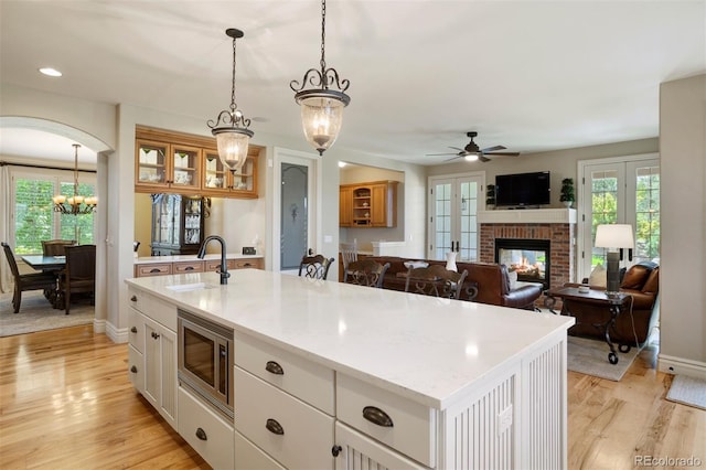 kitchen with sink, a center island with sink, a fireplace, ceiling fan with notable chandelier, and stainless steel microwave