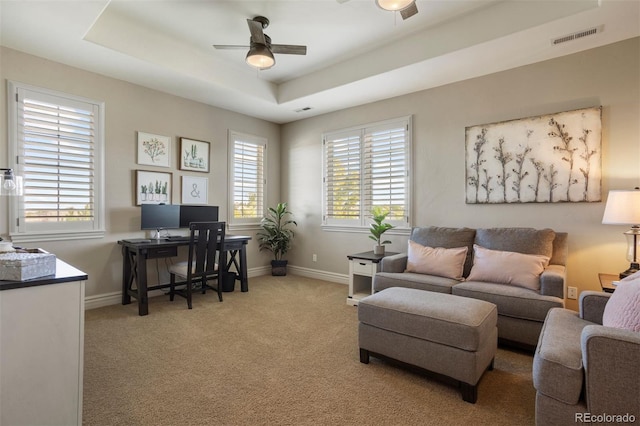 carpeted office space featuring a tray ceiling and ceiling fan