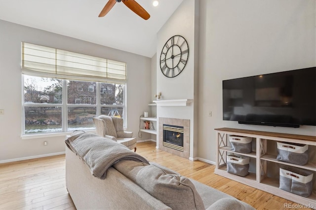 living room with a tile fireplace, high vaulted ceiling, light hardwood / wood-style flooring, and ceiling fan