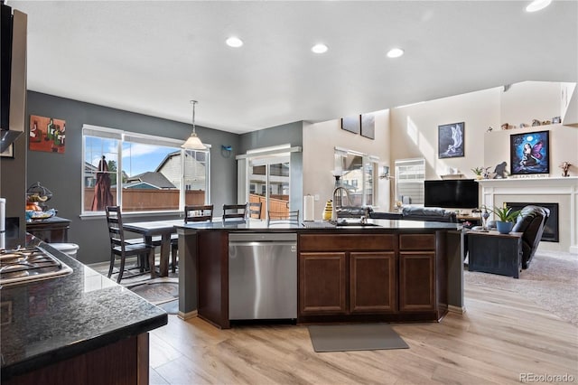 kitchen featuring stainless steel appliances, sink, light hardwood / wood-style floors, hanging light fixtures, and an island with sink