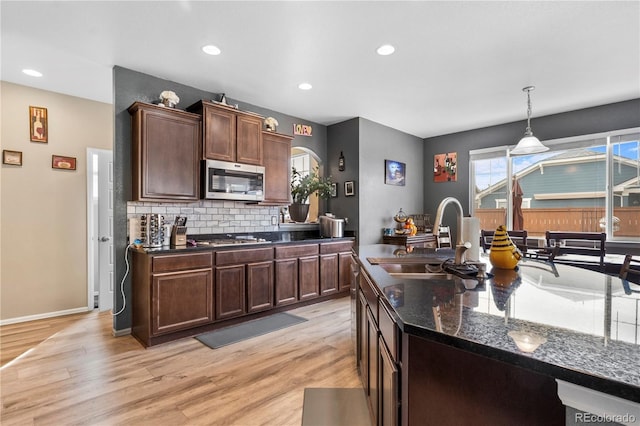 kitchen featuring appliances with stainless steel finishes, light wood-type flooring, tasteful backsplash, sink, and decorative light fixtures