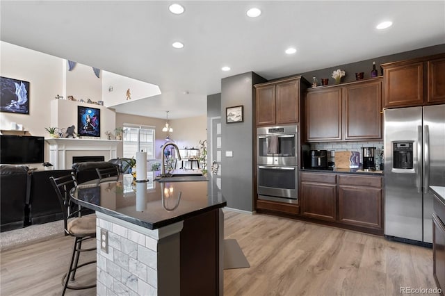 kitchen featuring a kitchen island with sink, a kitchen breakfast bar, sink, appliances with stainless steel finishes, and light hardwood / wood-style floors