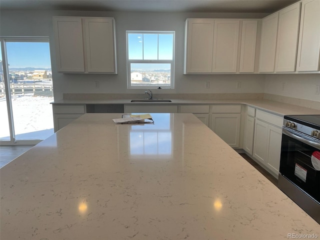 kitchen featuring white cabinets, sink, stainless steel range with electric cooktop, and light stone counters