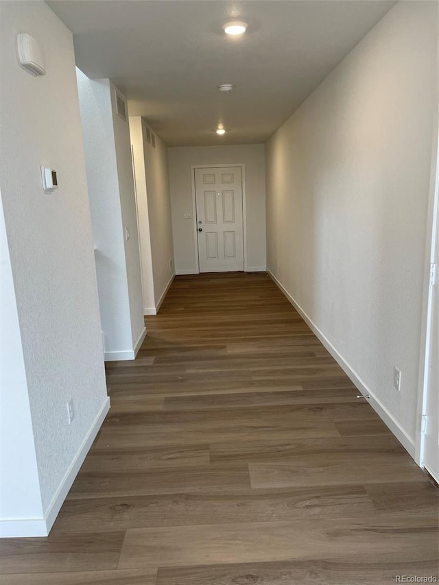 corridor featuring visible vents, baseboards, and wood finished floors