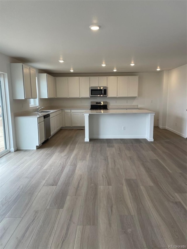 kitchen featuring recessed lighting, light countertops, appliances with stainless steel finishes, light wood-style floors, and a sink