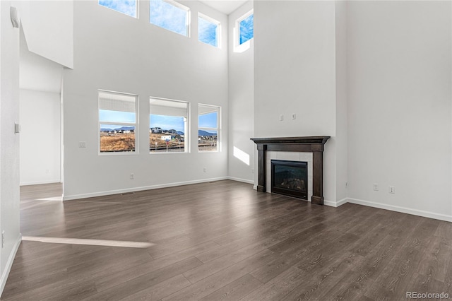 unfurnished living room with a tiled fireplace, a towering ceiling, and dark hardwood / wood-style flooring