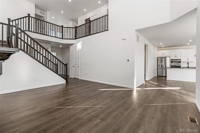 unfurnished living room featuring a high ceiling, dark wood-type flooring, and sink