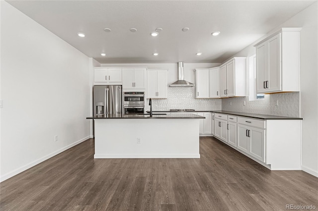 kitchen with stainless steel appliances, a center island with sink, wall chimney range hood, and white cabinets