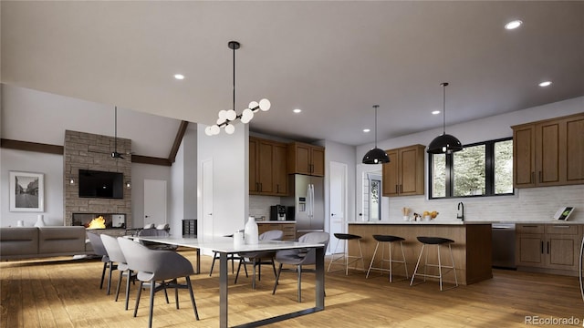 kitchen with appliances with stainless steel finishes, a stone fireplace, a breakfast bar area, hanging light fixtures, and kitchen peninsula