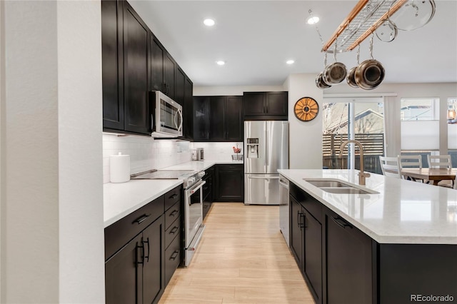 kitchen featuring sink, light hardwood / wood-style floors, an island with sink, decorative backsplash, and appliances with stainless steel finishes