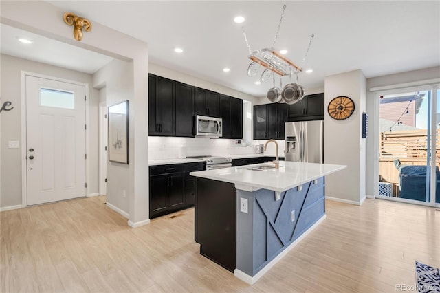 kitchen featuring stainless steel appliances, sink, light hardwood / wood-style floors, tasteful backsplash, and a kitchen island with sink