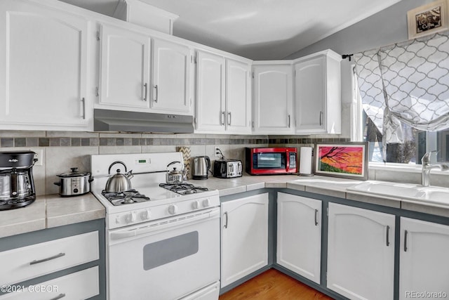 kitchen featuring gas range gas stove, a sink, light countertops, under cabinet range hood, and white cabinetry