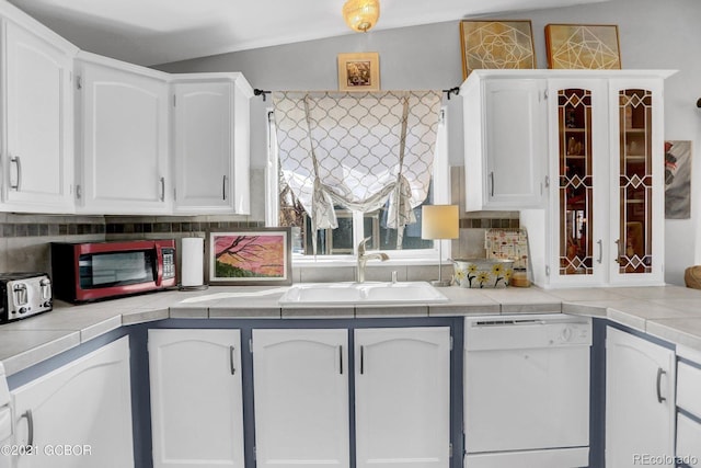 kitchen with white dishwasher, a sink, tile counters, white cabinets, and tasteful backsplash