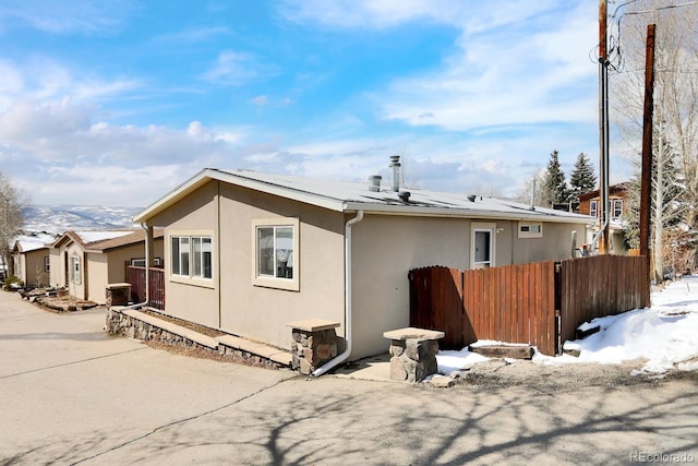 snow covered back of property with stucco siding and fence