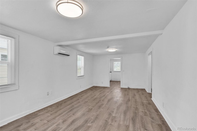 unfurnished room with an AC wall unit, light hardwood / wood-style floors, and plenty of natural light