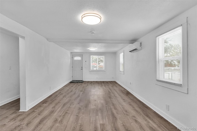 spare room featuring a wall unit AC, a wealth of natural light, a textured ceiling, and light wood-type flooring