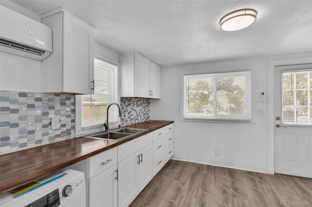 kitchen featuring butcher block counters, sink, a wall mounted AC, light wood-type flooring, and decorative backsplash