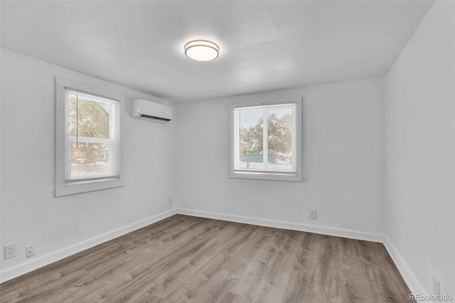 unfurnished room with a wealth of natural light, a wall unit AC, and light hardwood / wood-style flooring