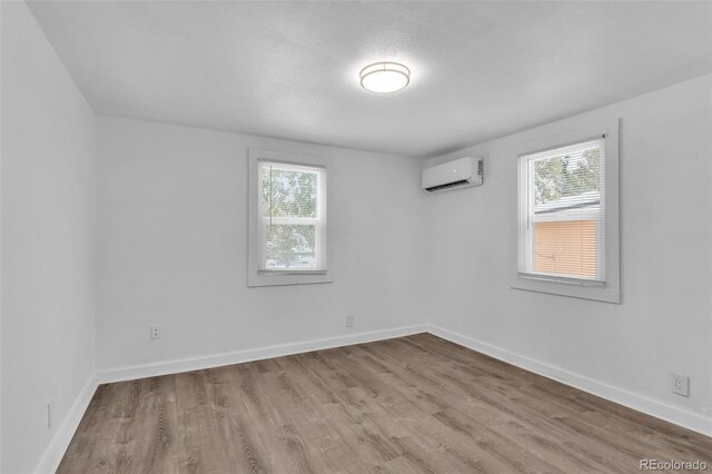 spare room with a wall mounted AC, a healthy amount of sunlight, and light wood-type flooring