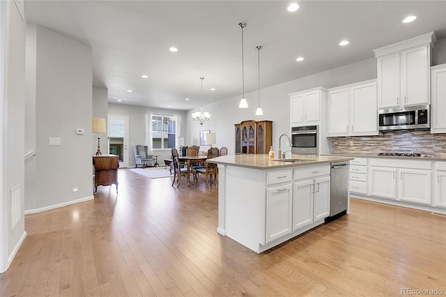 kitchen with light hardwood / wood-style floors, decorative light fixtures, appliances with stainless steel finishes, and a kitchen island with sink