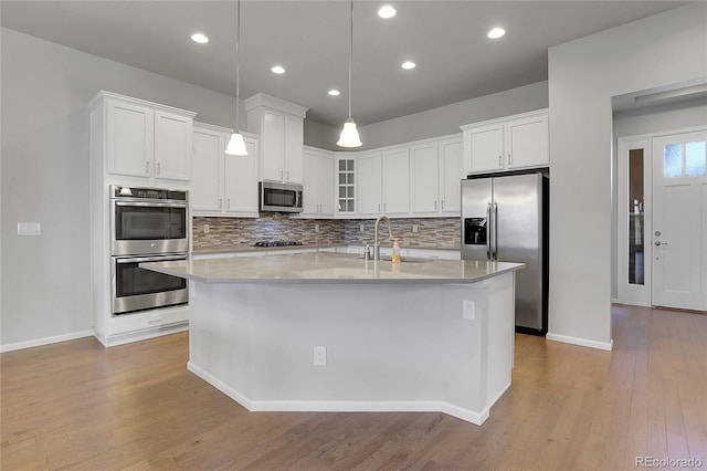 kitchen with white cabinets, hanging light fixtures, sink, light hardwood / wood-style flooring, and appliances with stainless steel finishes