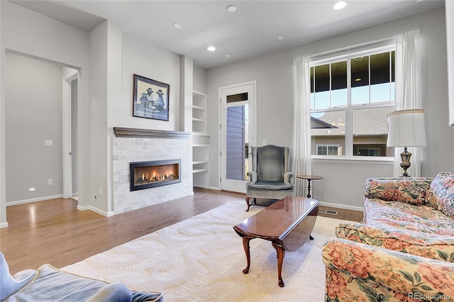 living room featuring a brick fireplace, built in features, and wood-type flooring