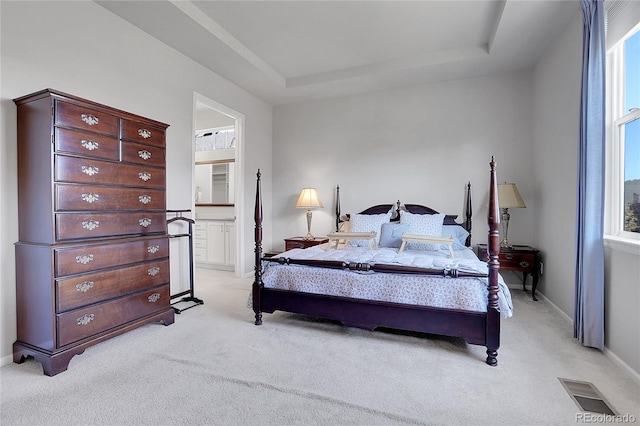 bedroom featuring light colored carpet, connected bathroom, multiple windows, and a tray ceiling