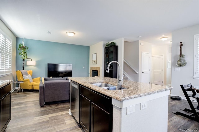 kitchen featuring a sink, light wood-style floors, stainless steel dishwasher, light stone countertops, and an island with sink