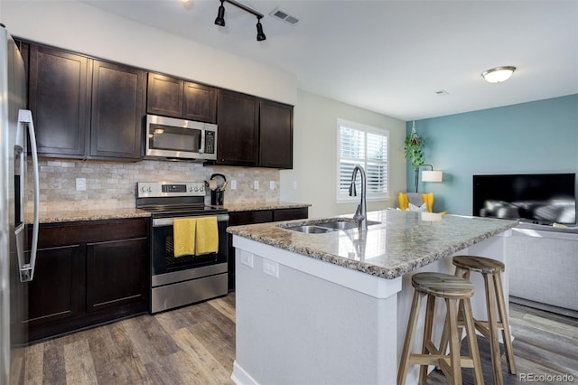 kitchen featuring stainless steel appliances, a sink, visible vents, dark wood-style floors, and a kitchen bar