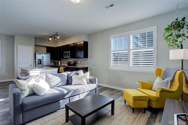 living room with track lighting, visible vents, baseboards, and wood finished floors