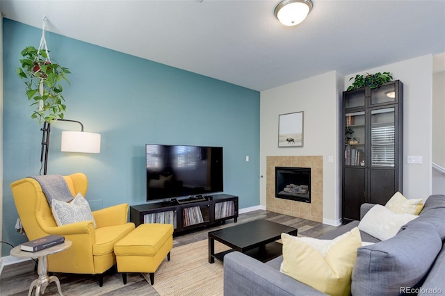 living area with a tile fireplace, baseboards, and wood finished floors