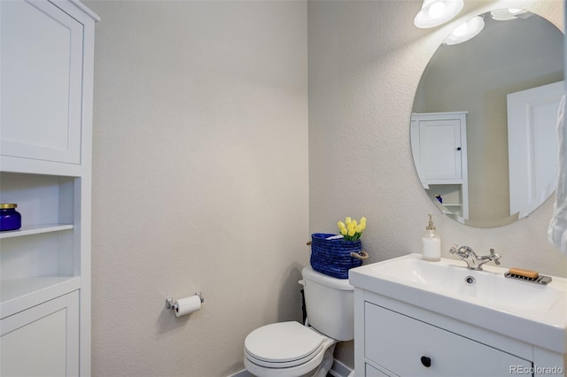 half bathroom featuring toilet, a textured wall, and vanity