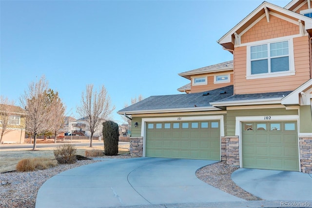 view of front facade featuring stone siding, roof with shingles, and driveway