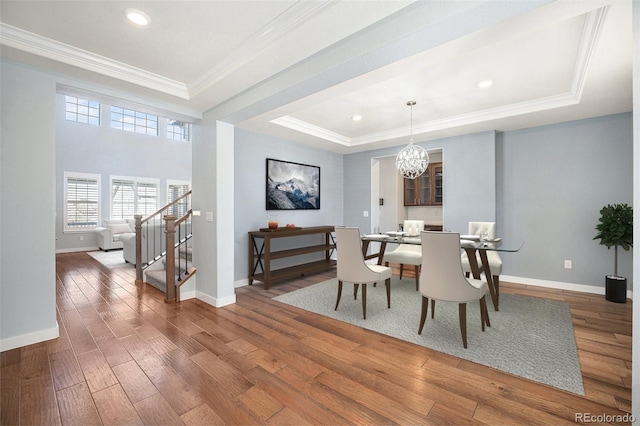 dining space with a chandelier, stairway, wood-type flooring, a raised ceiling, and crown molding