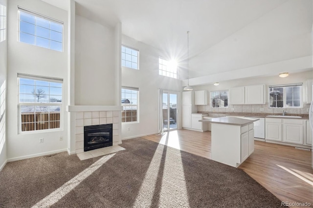 kitchen featuring hanging light fixtures, dishwasher, a tile fireplace, a kitchen island, and white cabinets