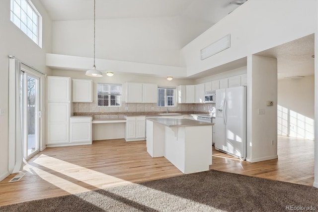 kitchen featuring white appliances, light hardwood / wood-style flooring, white cabinetry, hanging light fixtures, and a center island