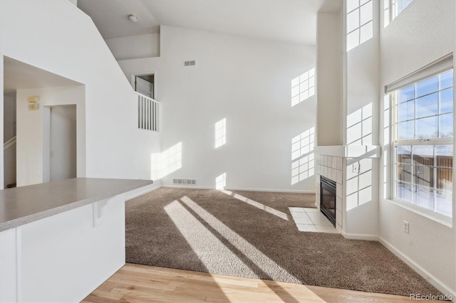 unfurnished living room with light carpet, a fireplace, and high vaulted ceiling