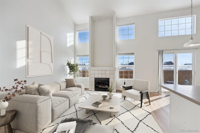 living room featuring plenty of natural light, light hardwood / wood-style floors, a tile fireplace, and a high ceiling