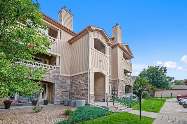 view of front of house with a balcony, stone siding, central AC, and a chimney