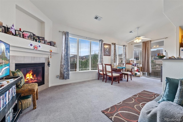 living room with visible vents, ceiling fan, a tiled fireplace, vaulted ceiling, and carpet floors
